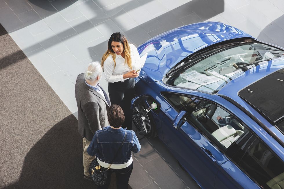 high angle view of saleswoman showing car to customers at showroom