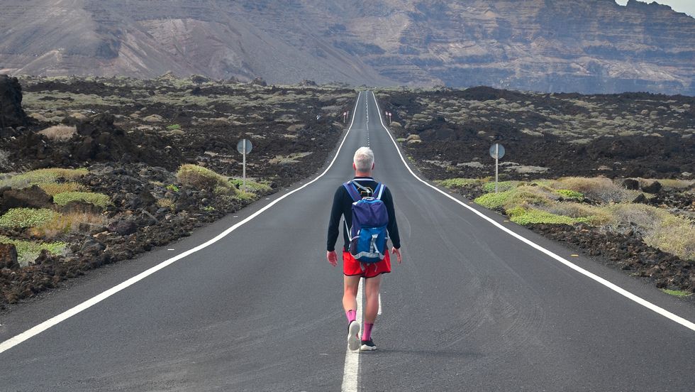 lonely oung man walking on an endless road in a volcanic landscape in lanzarote, canary islands