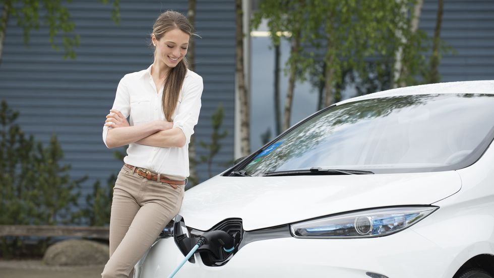 young woman with electric car at ev charging station