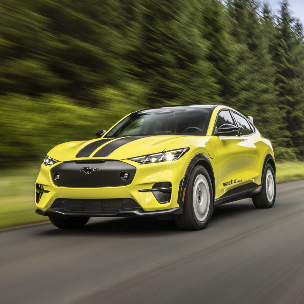 a ford mustang mach e rally shown in yellow speeding down a tree lined country road